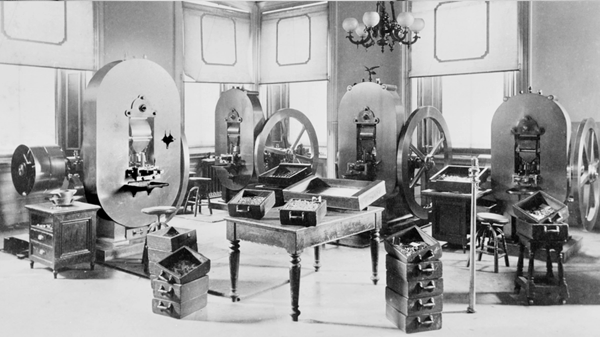 Figure 5. These presses are the type used to strike silver dollars in the late 19th and early 20th century at the U. S. Mint. The boxes contain freshly-struck Morgan-type silver dollars from the mid-1880’s. The boxes on the floor to the right of center contain misstruck coins. By 1905 the mint had converted its presses to electric operation. (Photo courtesy Library of Congress.)